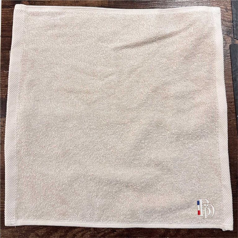 Serviette blanc cassé Barber District avec logo brodé en bas à droite.
