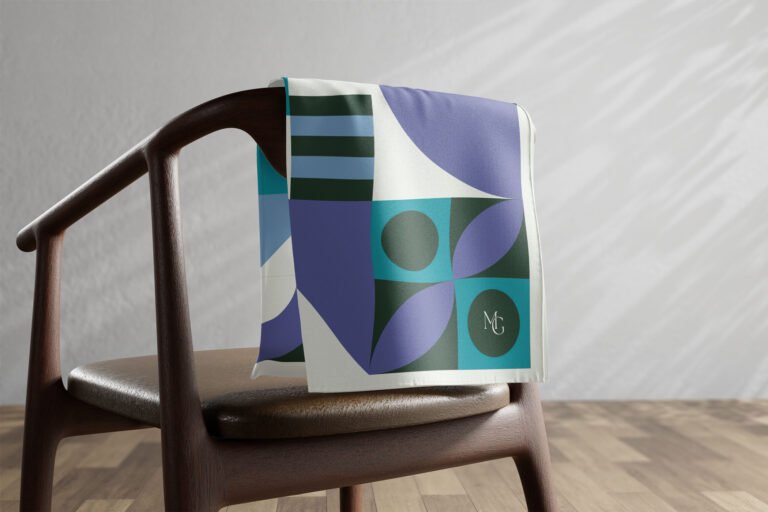 Carré de soie Maison Gabrielle à motif géométrique vert et violet posé sur une chaise.