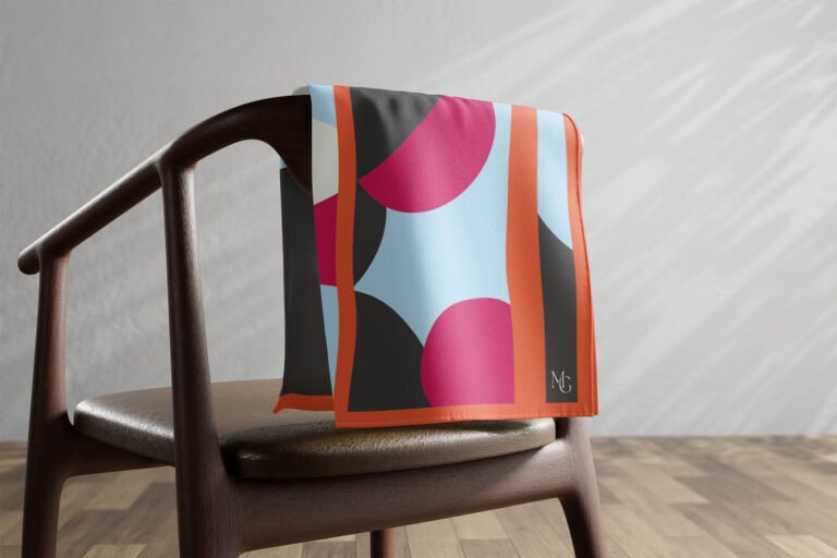 Carré de soie Maison Gabrielle à motif rose, bleu et orange posé sur une chaise.