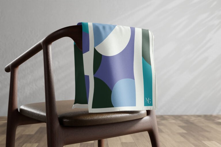 Carré de soie Maison Gabrielle à motif vert, bleu et blanc posé sur une chaise.