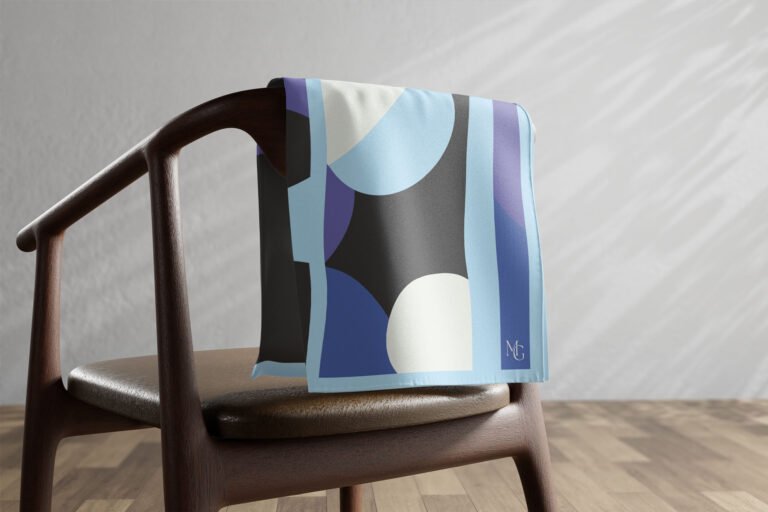 Carré de soie Maison Gabrielle à motif bleu, noir et blanc posé sur une chaise.